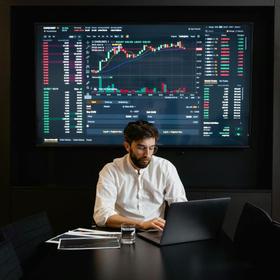 A stock trader analyzes cryptocurrency data on a laptop with graphs and charts on a screen.